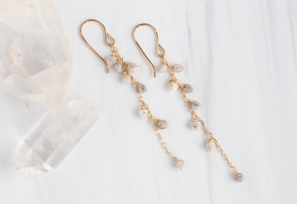 Yellow Gold Rough Diamond Cascade Earrings hanging on white marble tile