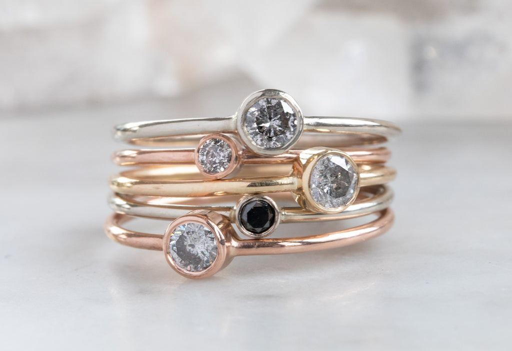 Teensy Custom Diamond Stacking Rings stacked on top of each other on white marble tile
