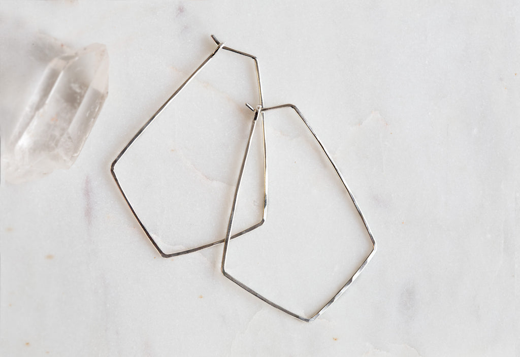White Gold Hexagon Hoop Earrings on white marble tile