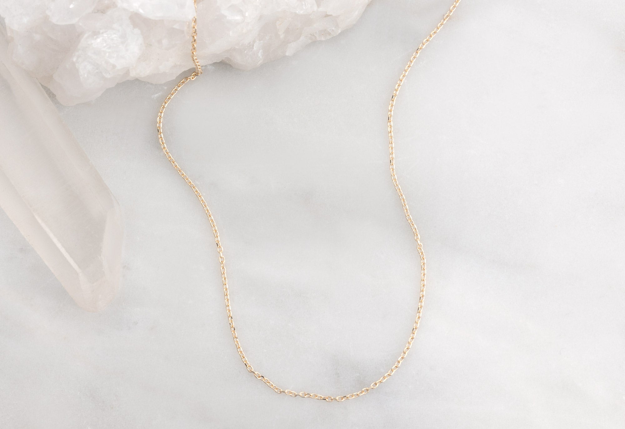 Yellow Gold Diamond-Cut Cable Chain Charm Necklace on White Marble Tile
