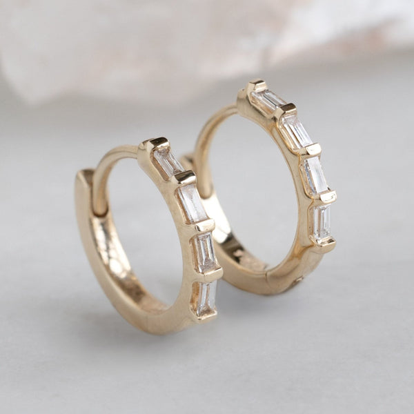 The Baguette White Diamond Huggie Hoops in 14K Yellow Gold on White Marble