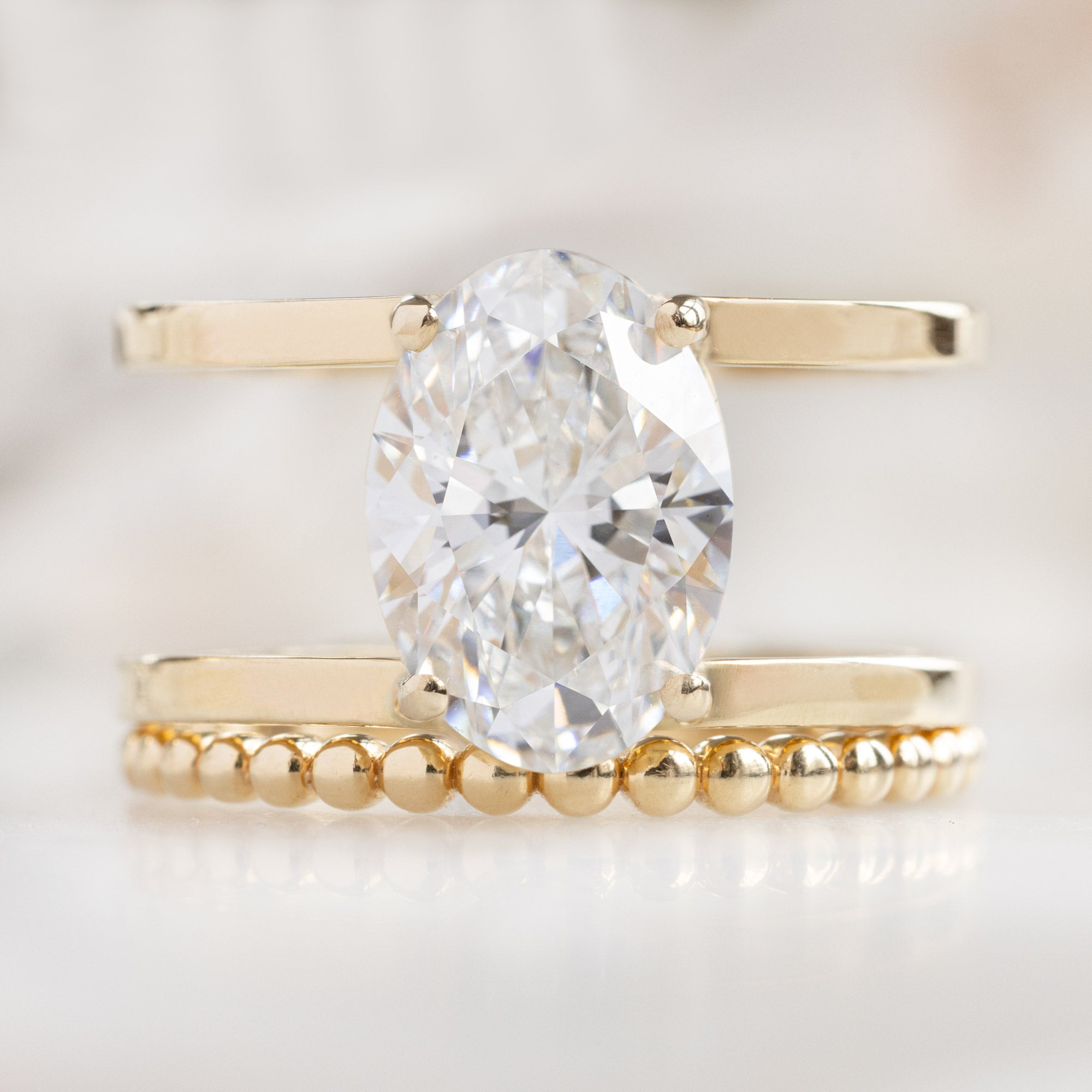 The Poppy Ring with a 3.06ct Oval Lab Grown White Diamond in 14K Yellow Gold Stacked with the Beaded Stacking Band