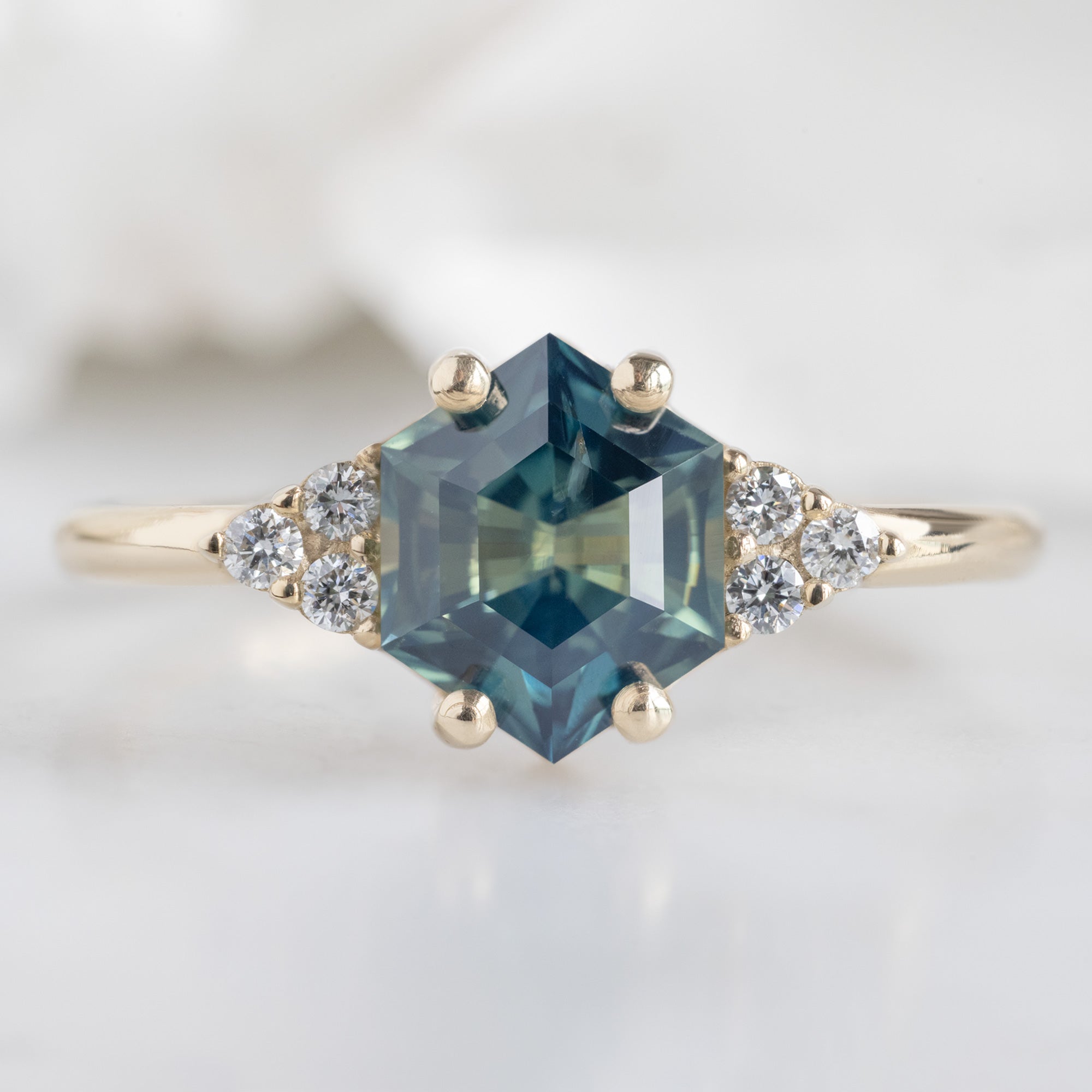 The Ivy Ring with a 1.37ct Hexagon Parti Sapphire in 14K Yellow Gold on white marble