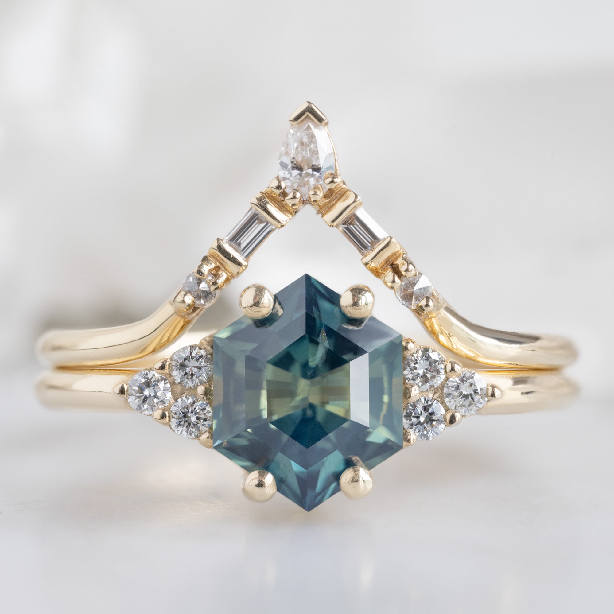The Ivy Ring with a 1.37ct Hexagon Parti Sapphire in 14K Yellow Gold stacked with the White Diamond Tiara Stacking Band on White Marble