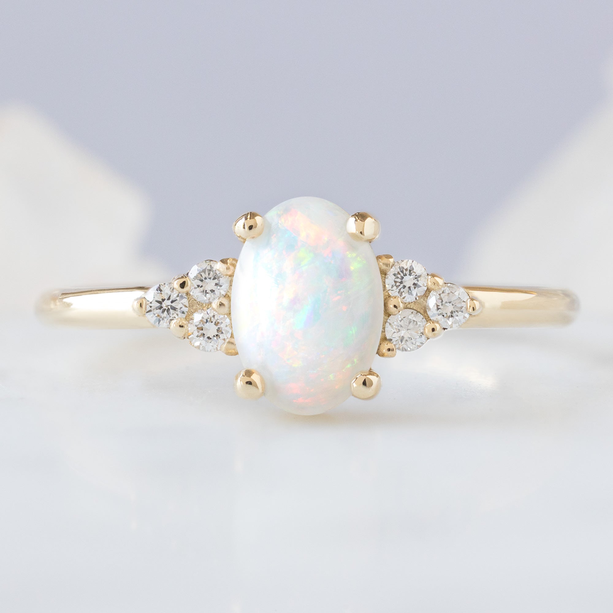 The Ivy Ring with a 0.44ct Oval Australian Opal in 14K Yellow Gold on Pale Blue Background