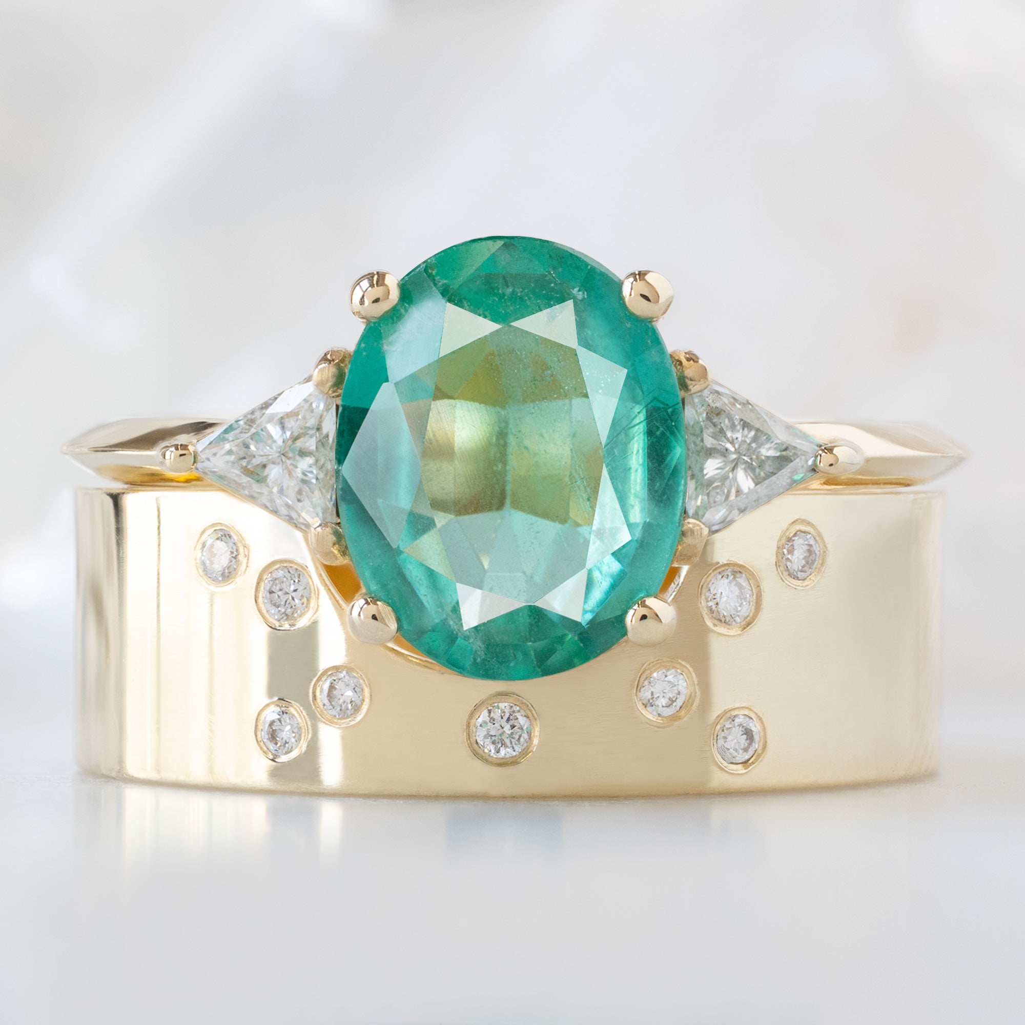 The Jade Ring with a 1.27ct Oval Emerald in 14K Yellow Gold Stacked with the Constellation Arc Stacking Band on White Marble Surface