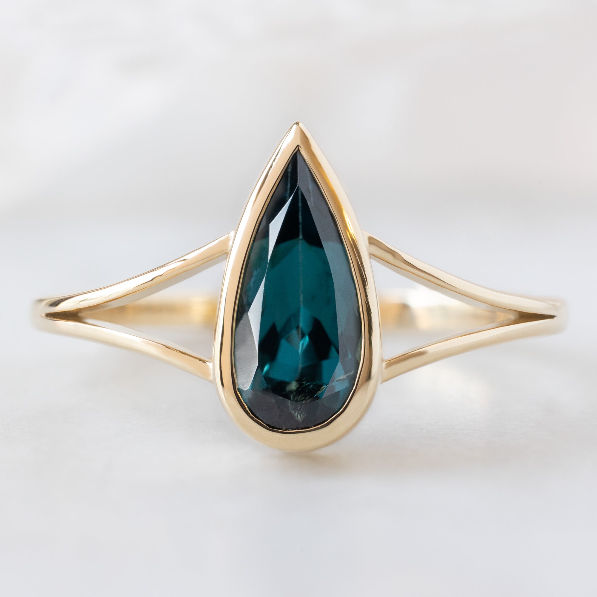 The Magnolia Ring with a 1.48ct Pear Blue Sapphire in 14K Yellow Gold on White Marble Surface