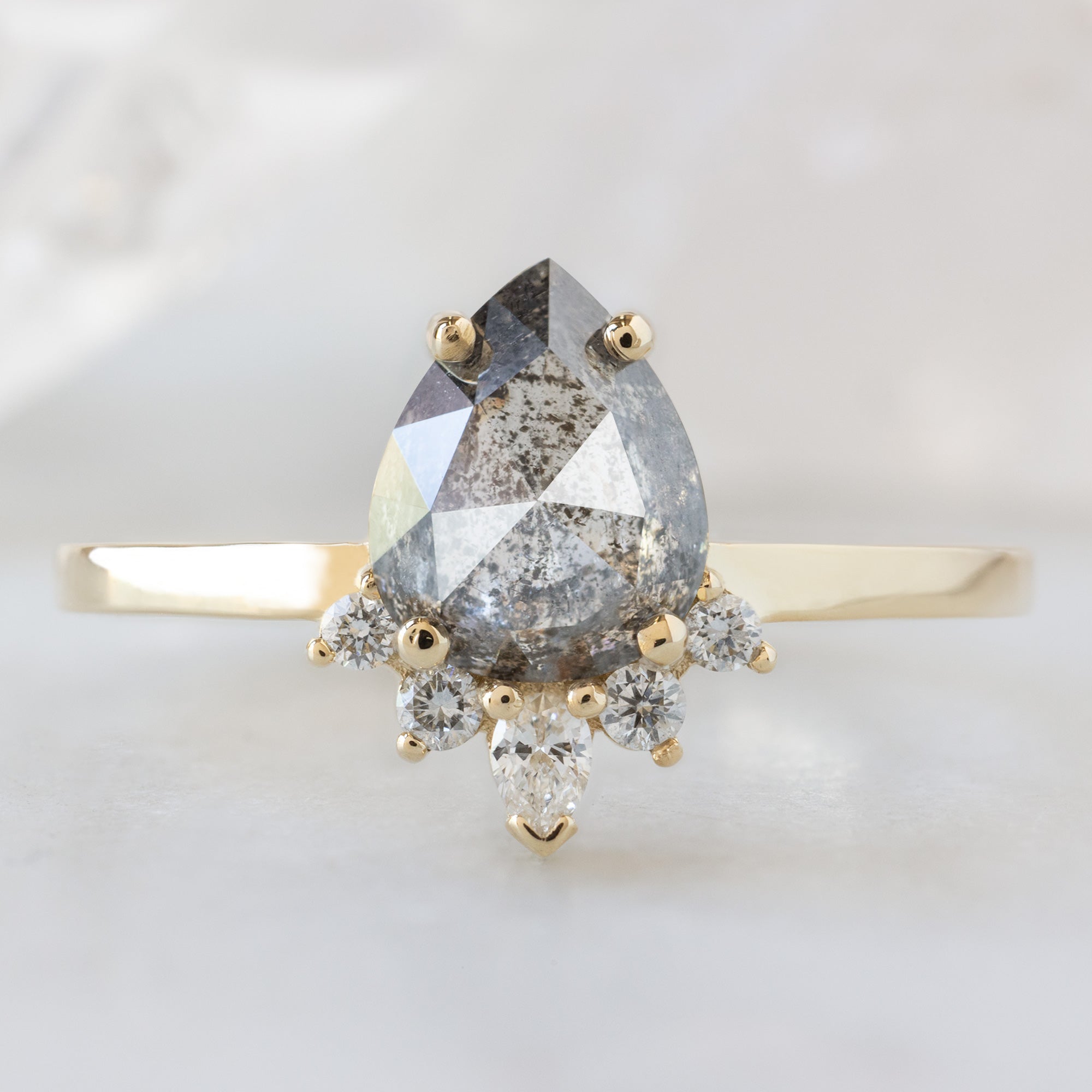The Aster Ring with a 1.35ct Pear Salt and Pepper Diamond in 14K Yellow Gold on White Marble Surface