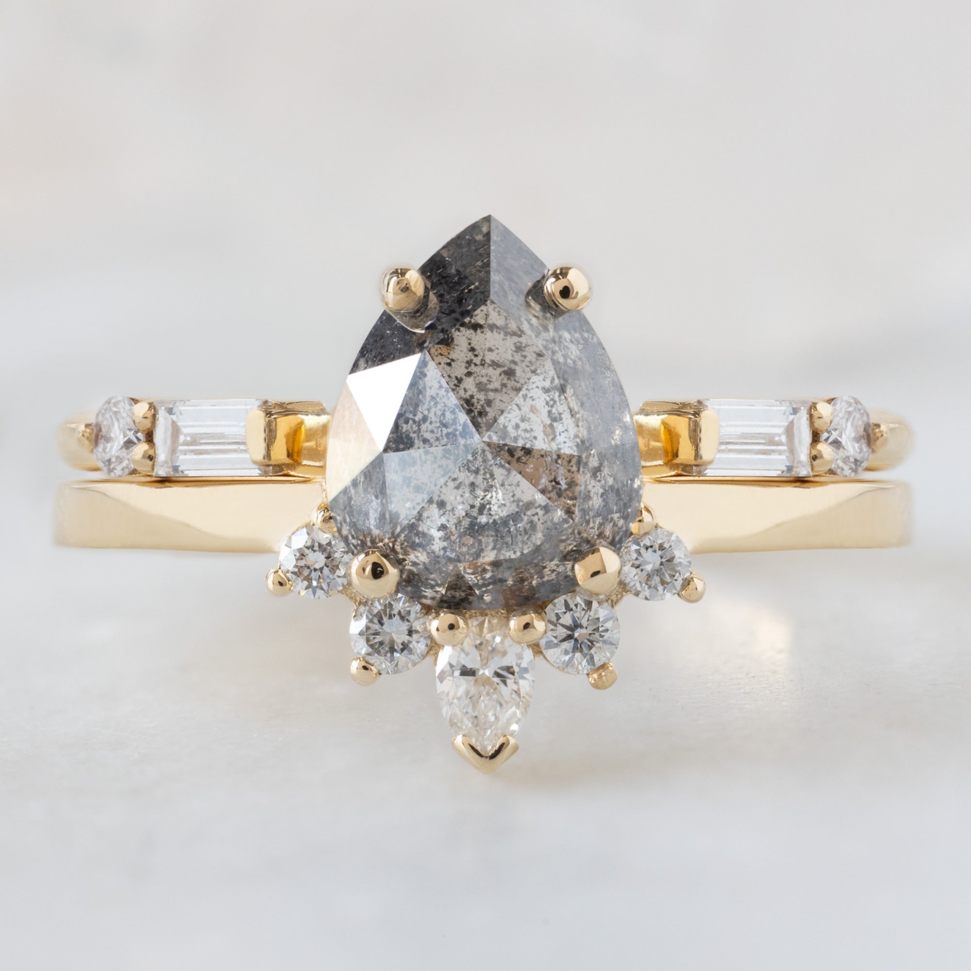 The Aster Ring with a 1.35ct Pear Salt and Pepper Diamond in 14K Yellow Gold Stacked with the Luxe Open Cuff Baguette Diamond Stacking Band on White Marble Surface