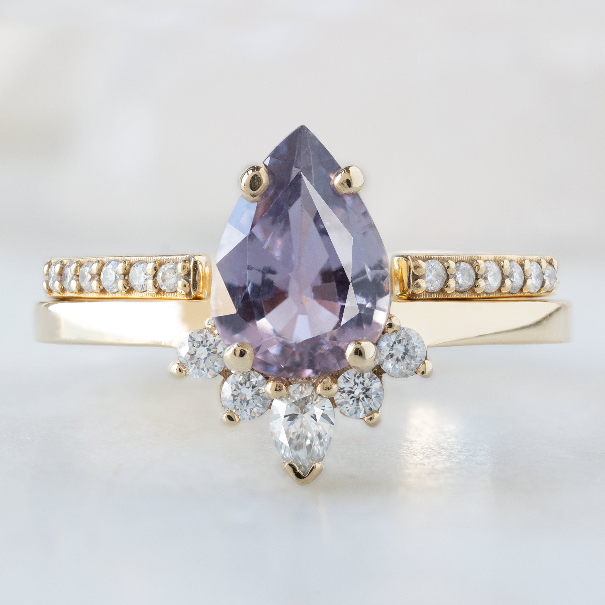 The Aster Ring with a 1.06ct Pear Purple Sapphire in 14K Yellow Gold Stacked with the Open Cuff White Diamond Pavé Stacking Band on White Marble Surface