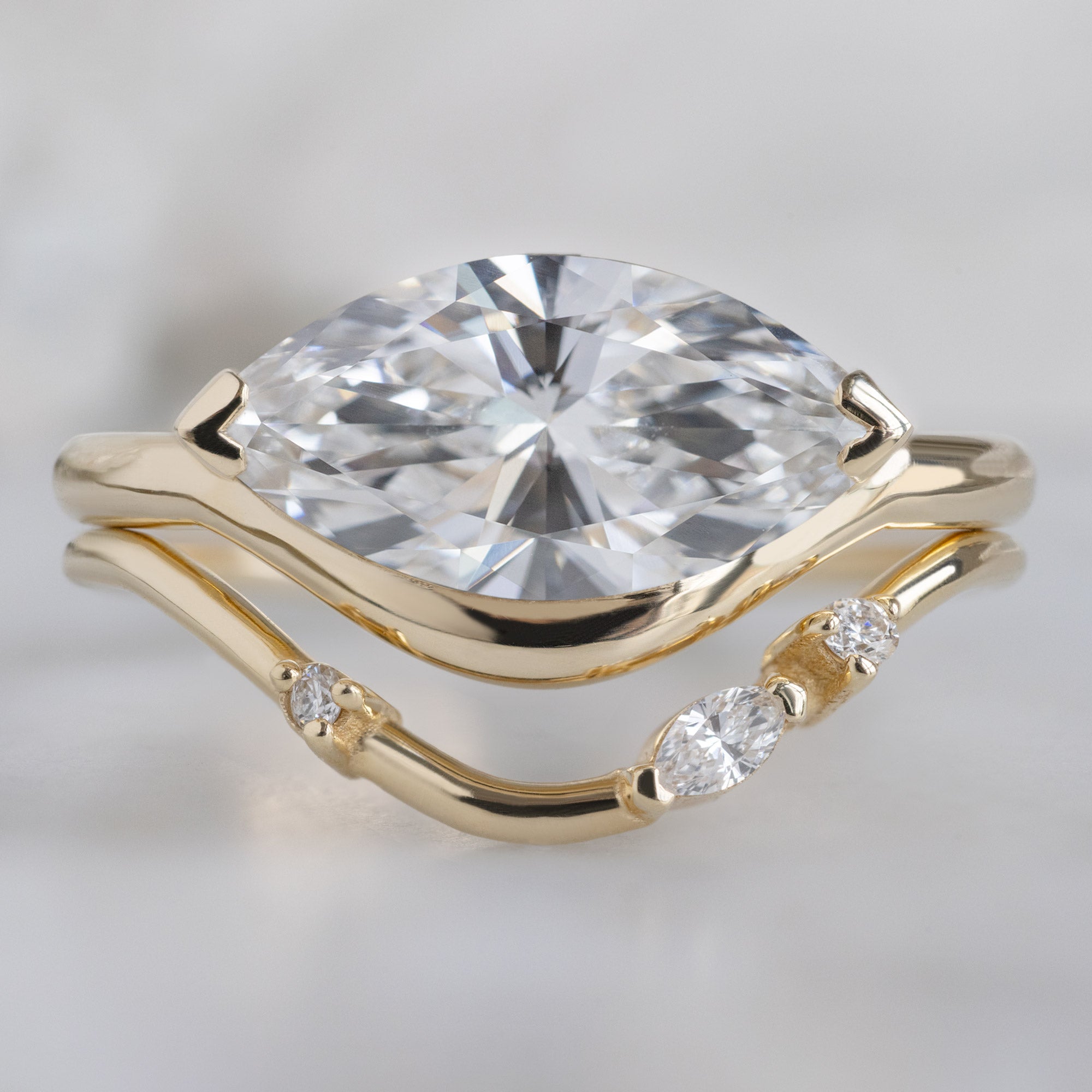 The Wave Ring with a 1.50ct Marquise Lab Grown White Diamond in 14K Yellow Gold on Model Stacked with the Asymmetrical Marquise Diamond Stacking Band on White Marble Surface