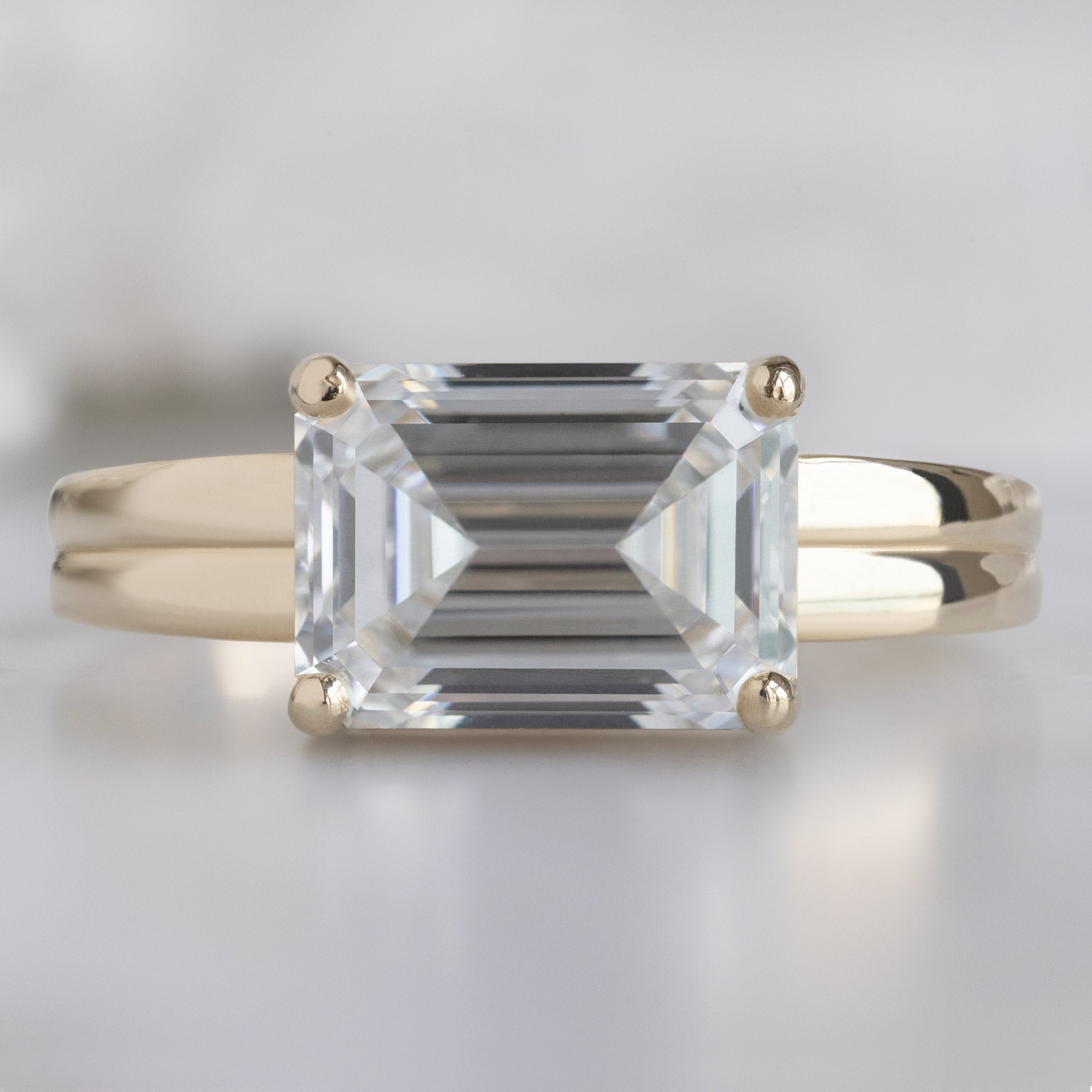 The Stratum Ring with a 1.96ct Emerald Cut Lab Grown White Diamond in 14K Yellow Gold on White Marble Surface