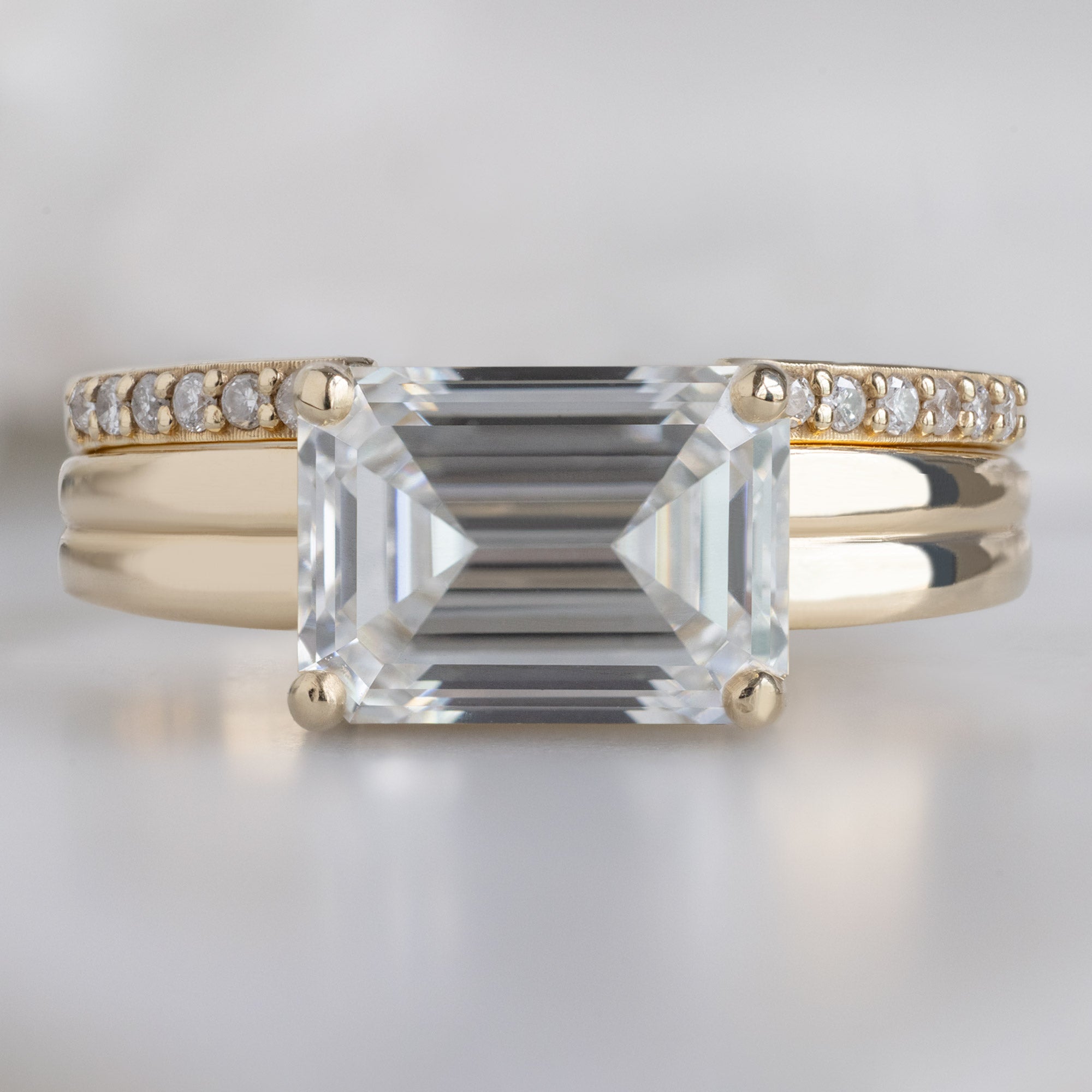 The Stratum Ring with a 1.96ct Emerald Cut Lab Grown White Diamond in 14K Yellow Gold Stacked with the Open Cuff White Diamond Pavé Stacking Band on White Marble Surface