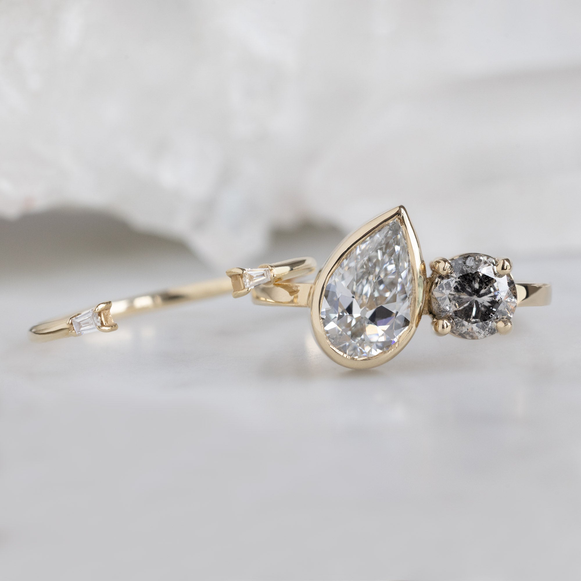 The You and Me Ring with a 1.25ct Pear Lab Grown White Diamond in 14K Yellow Gold Stacked with the Open Cuff White Diamond Baguette Stacking on White Marble