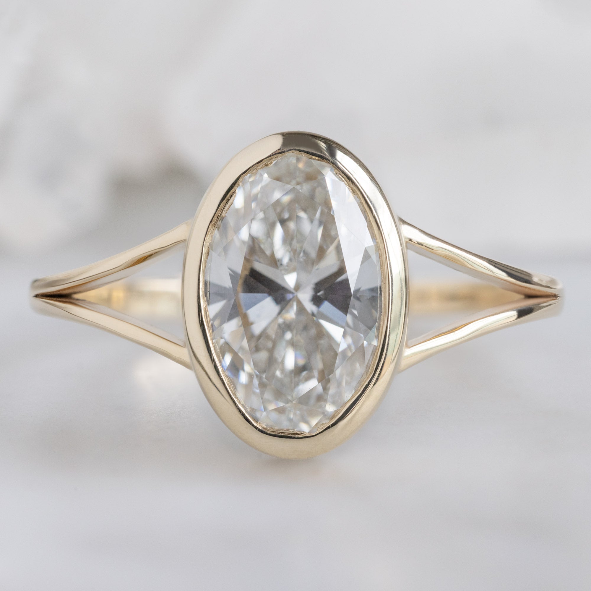 The Magnolia Ring with a 1.93ct Oval Lab Grown White Diamond in 14K Yellow Gold on White Marble Surface