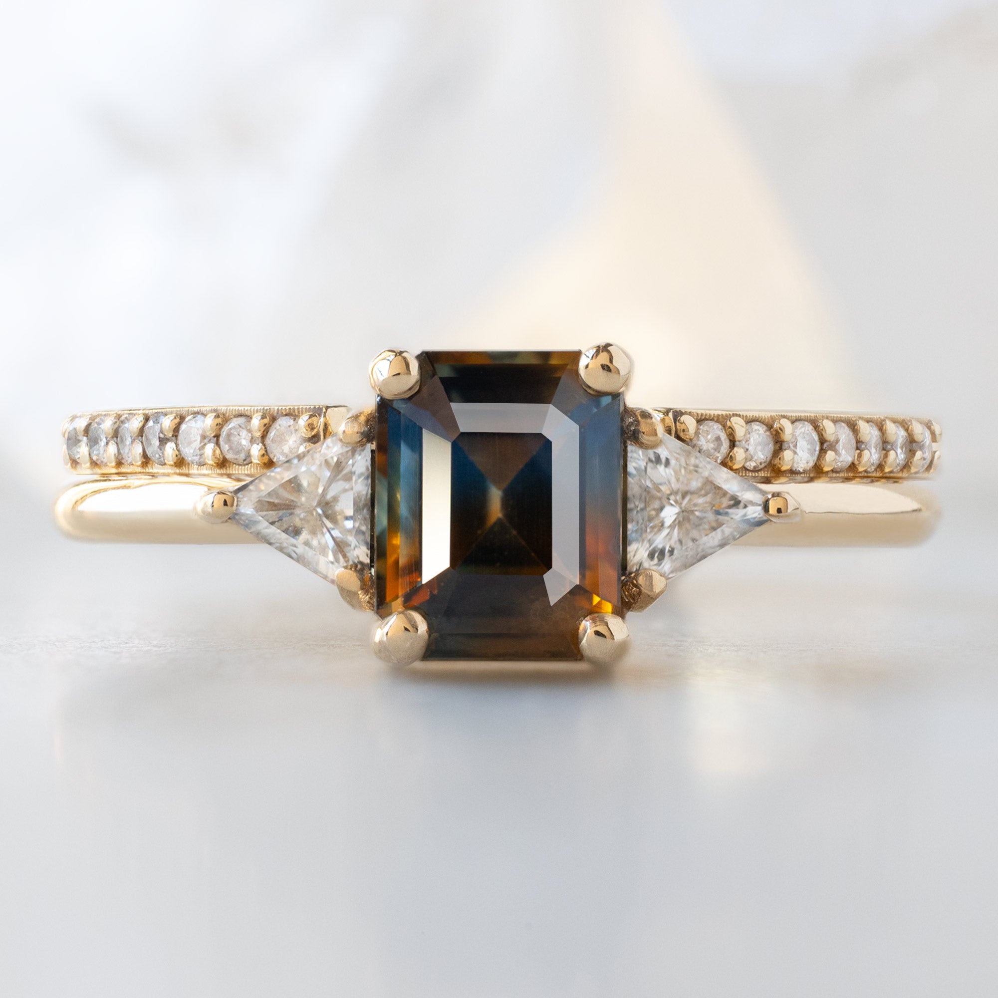 The Jade Ring with a 1.19ct Emerald Cut Parti Sapphire in 14K Yellow Gold Stacked with the Open Cuff White Diamond Pavé Stacking Band on White Marble Surface