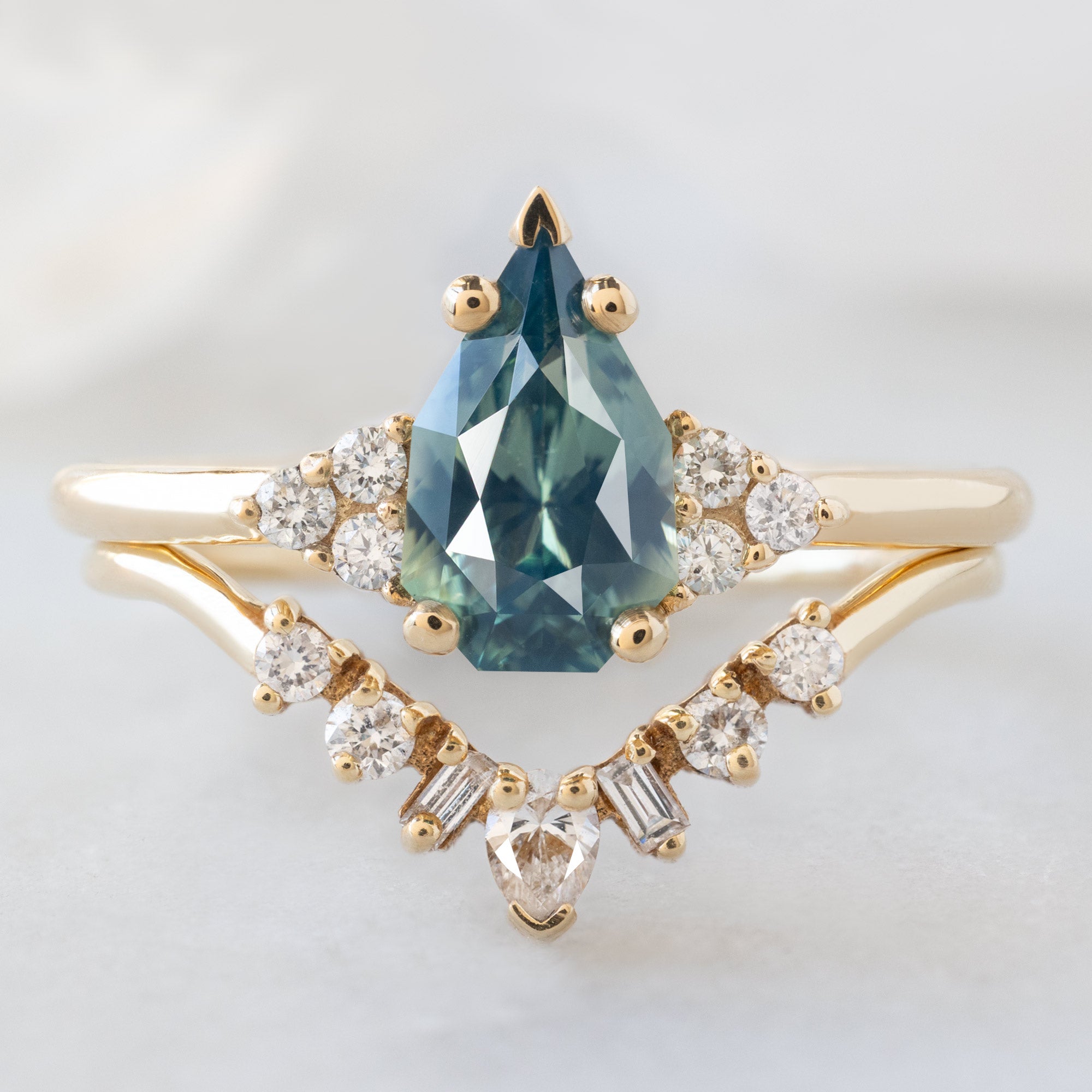The Ivy Ring with a 1.07ct Geometric Montana Bicolor Sapphire in 14K Yellow Gold Stacked with the Geometric White Diamond Sunburst Stacking Band on White Marble Surface