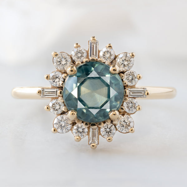 The Compass Ring with a 1.66ct Round Blue Sapphire in 14K Yellow Gold on White Marble Surface