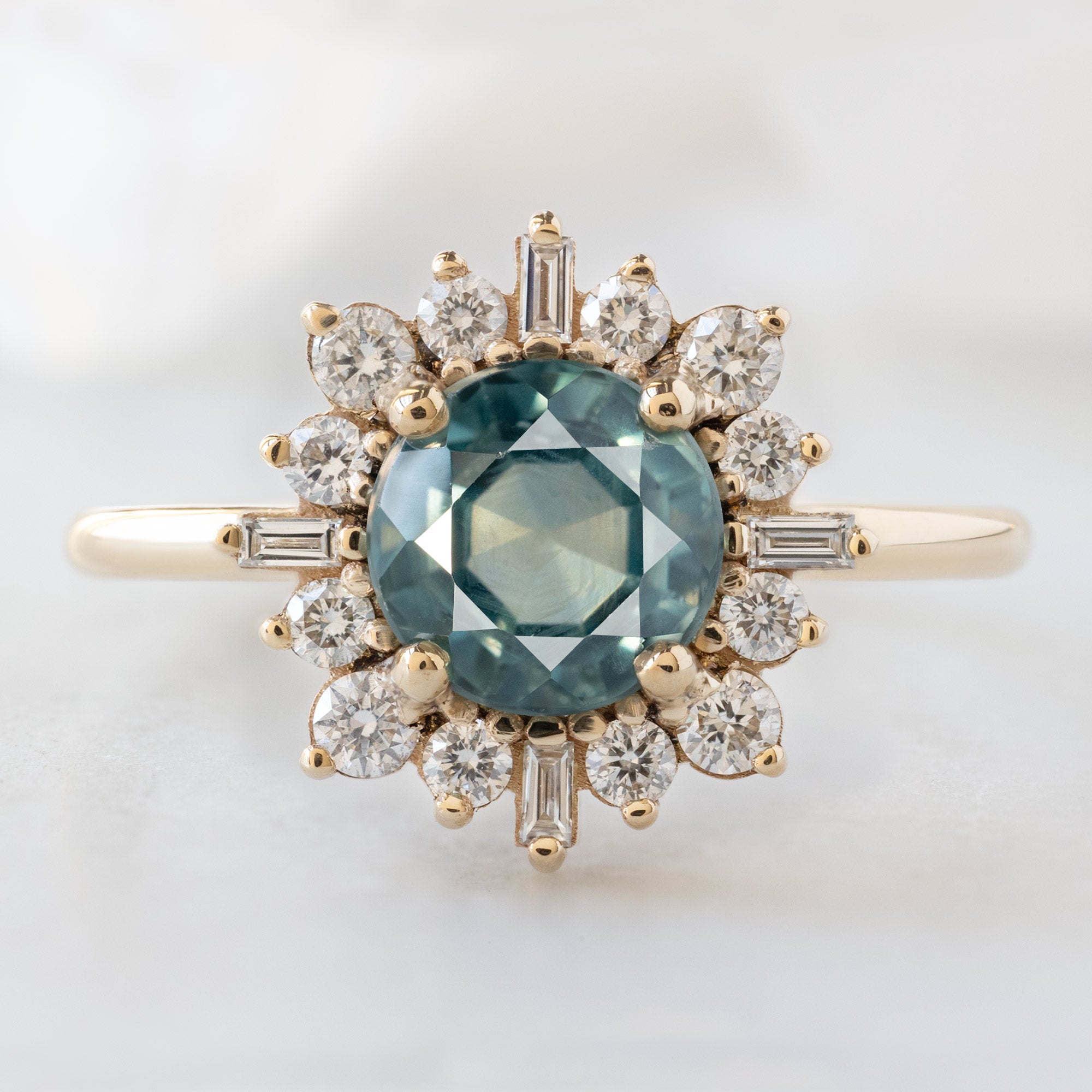 The Compass Ring with a 1.66ct Round Blue Sapphire in 14K Yellow Gold on White Marble Surface