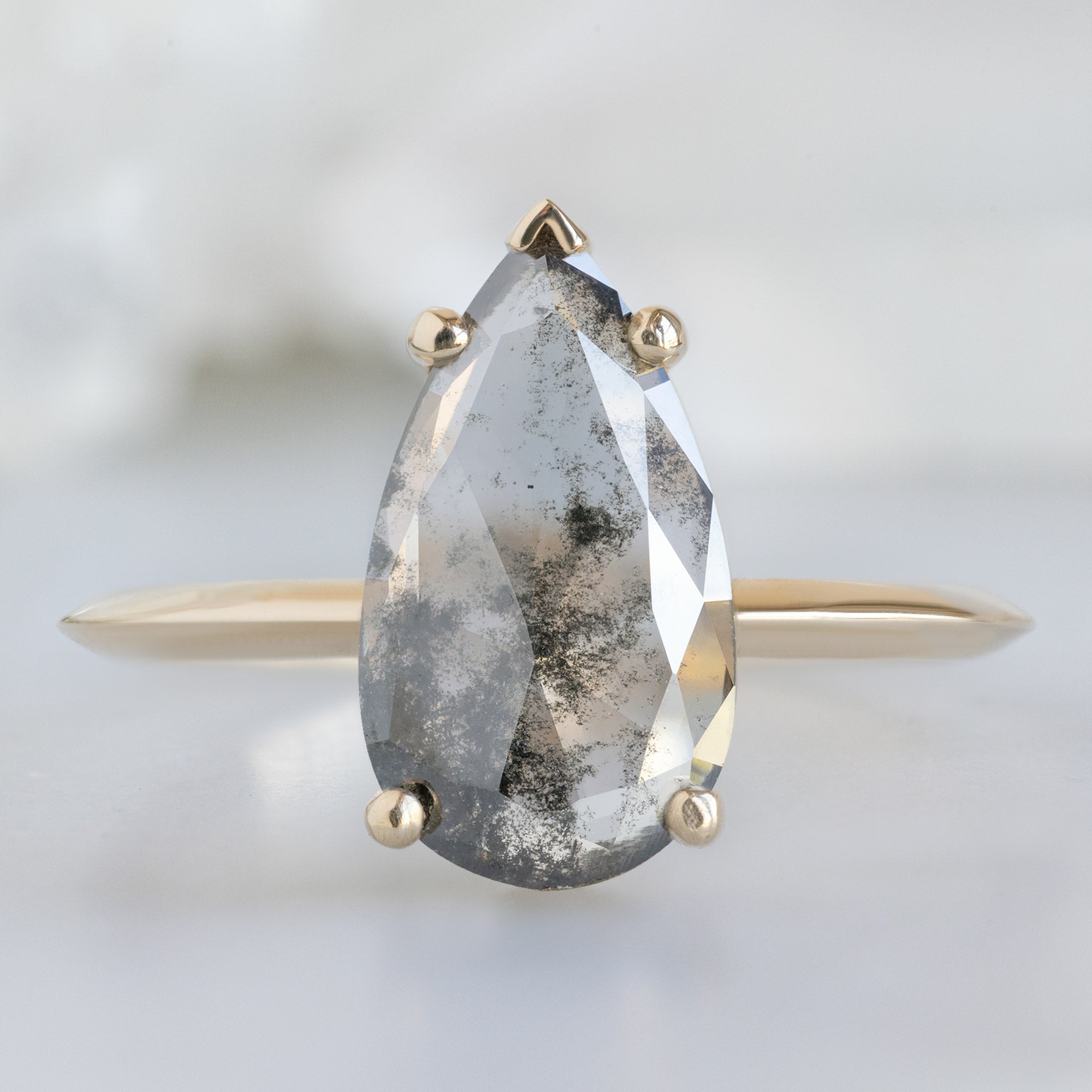 The Sage Ring with a 1.19ct Pear Lab Grown Salt and Pepper Diamond in 14K Yellow Gold on White Marble Surface