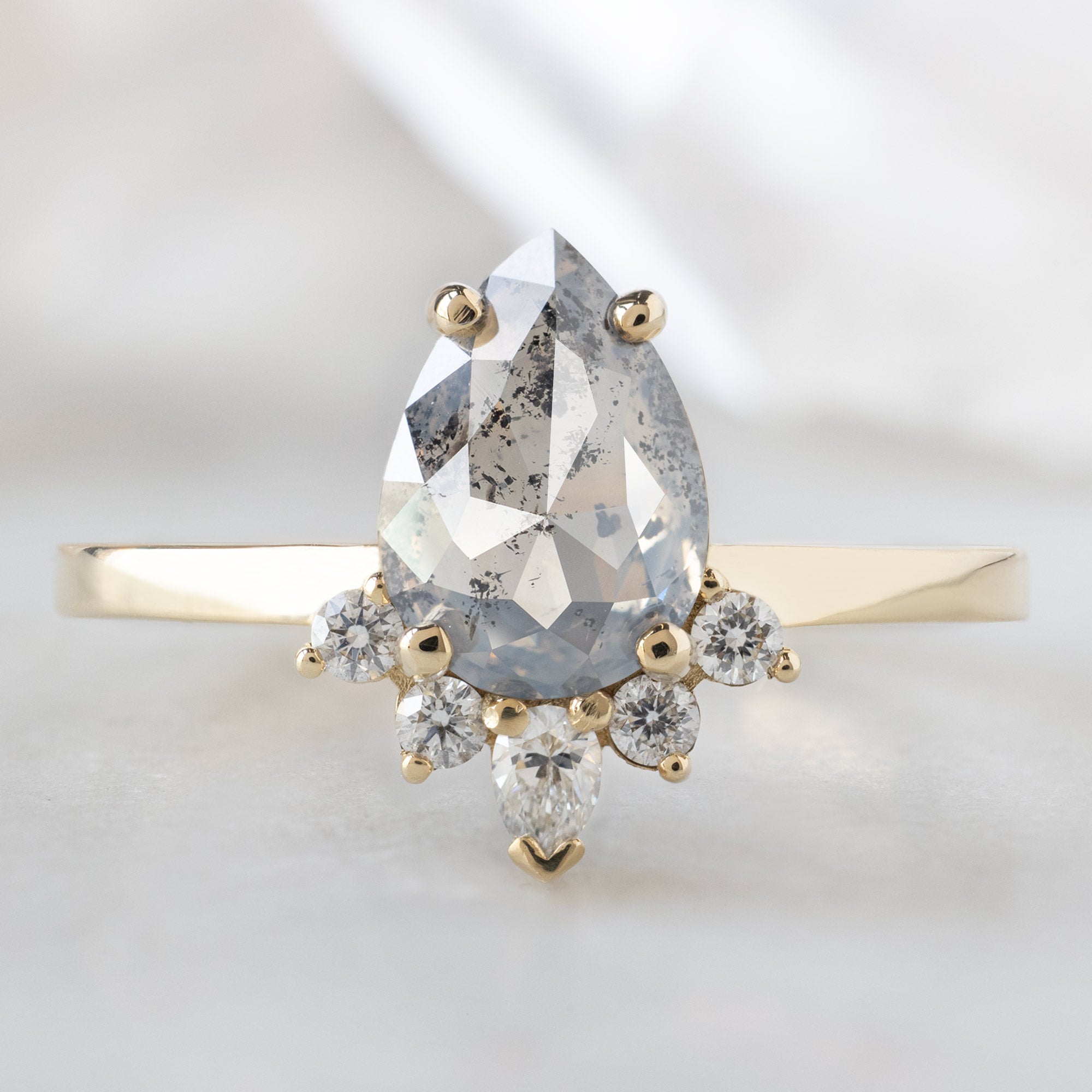 The Aster Ring with a 1.19ct Pear Salt and Pepper Diamond in 14K Yellow Gold on White Marble