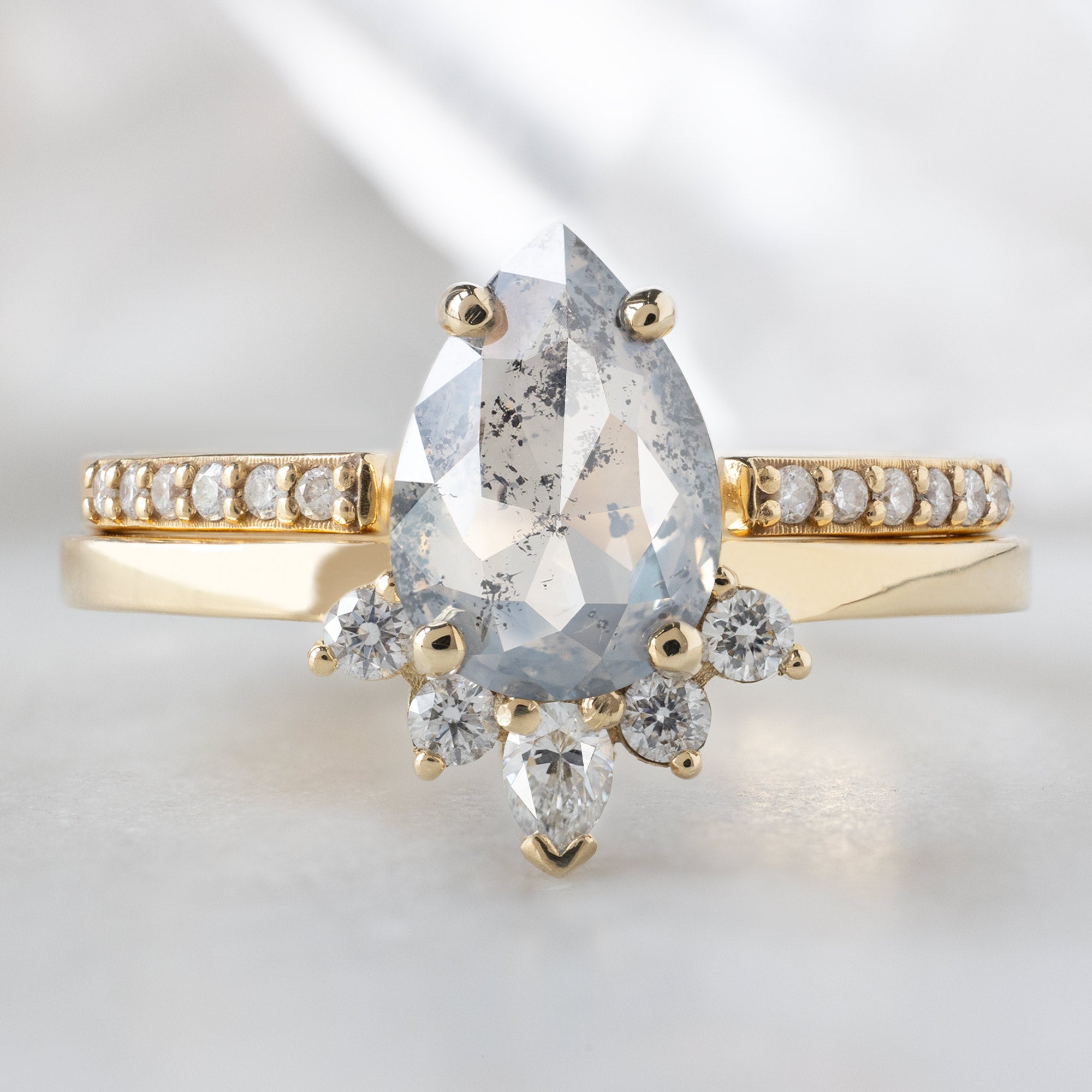 The Aster Ring with a 1.19ct Pear Salt and Pepper Diamond in 14K Yellow Gold Stacked with the Open Cuff White Diamond Pavé Stacking Band on White Marble Background