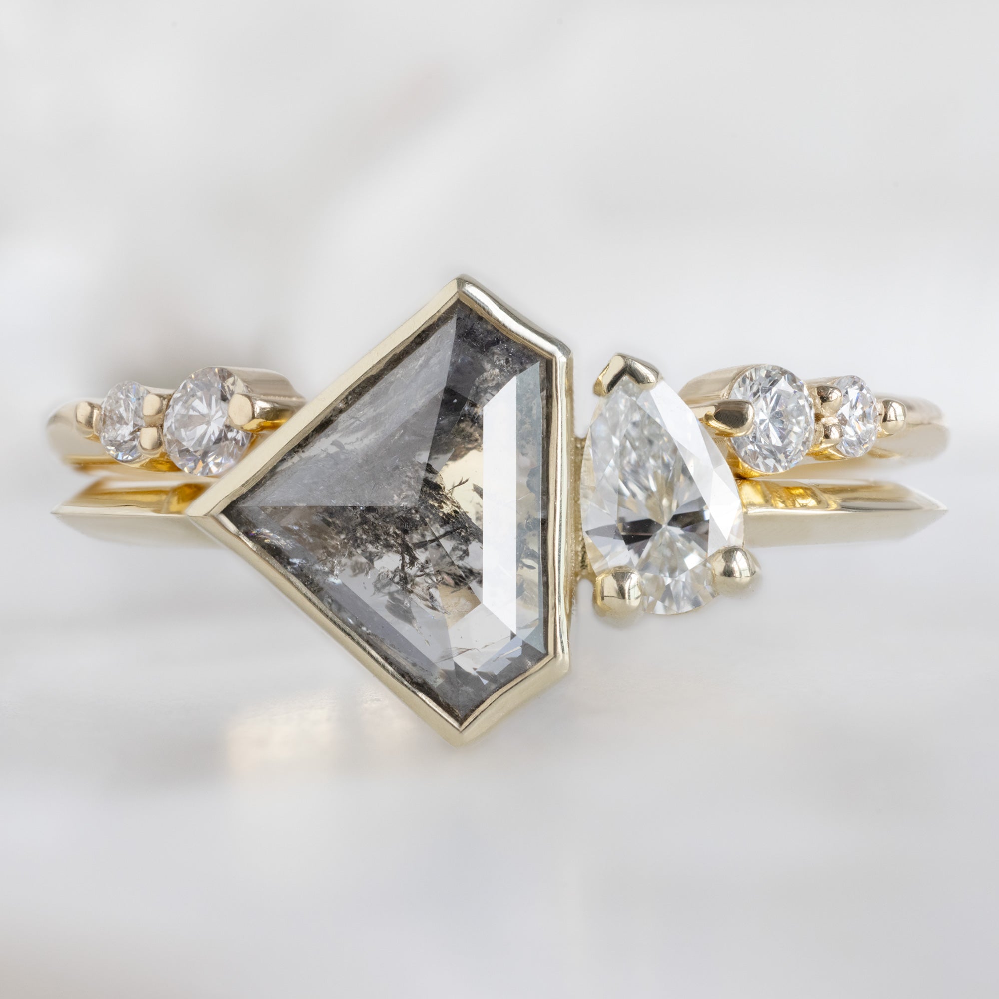 The You and Me Ring with a 1.35ct Shield Salt and Pepper in 14K Yellow Gold Stacked with the Luxe Open Cuff White Diamond Stacking Band on White Marble Surface