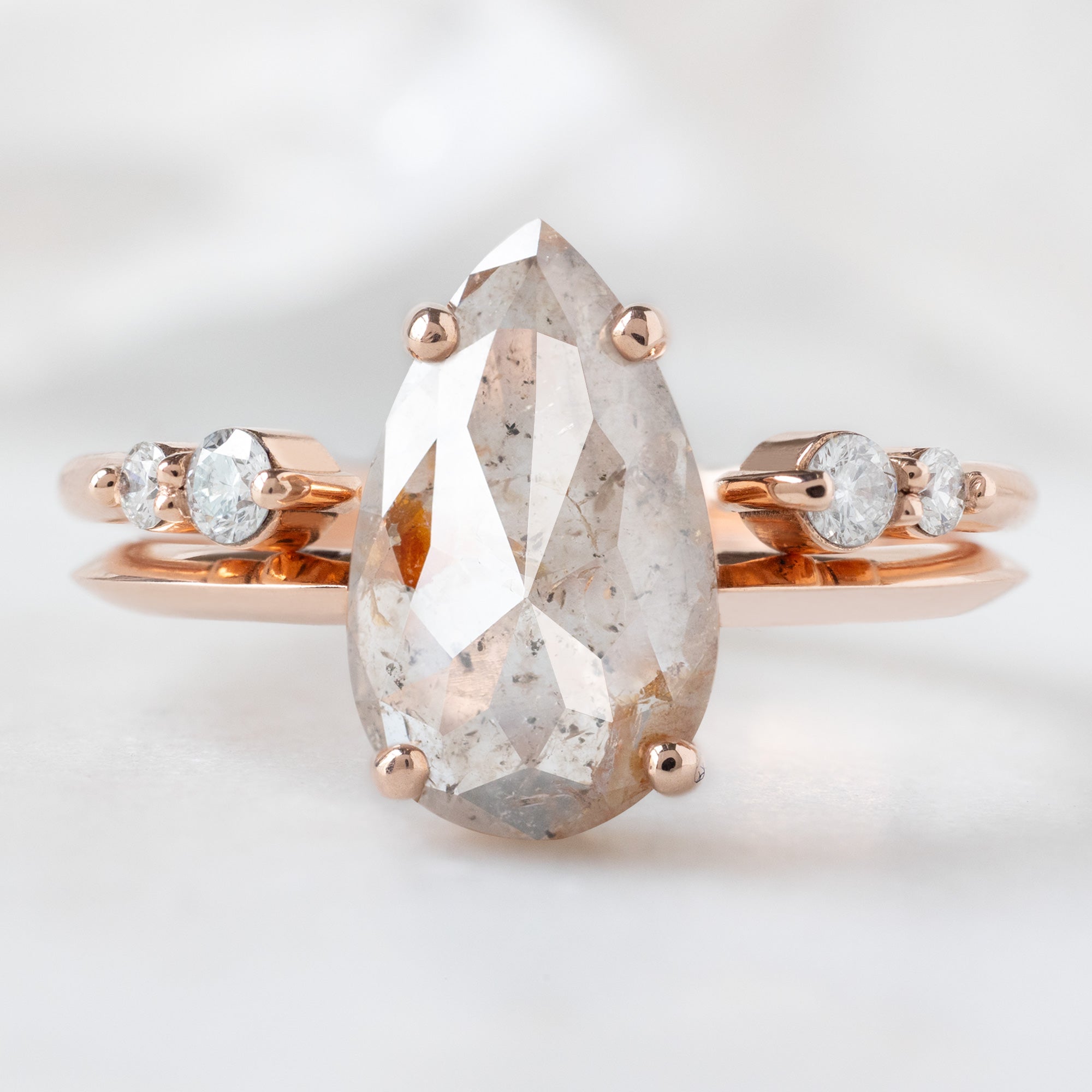 The Bryn Ring with a 1.76ct Pear Pink Diamond in 14K Rose Gold Stacked with the Luxe Open Cuff Round White Diamond Stacking Band on White Marble Surface