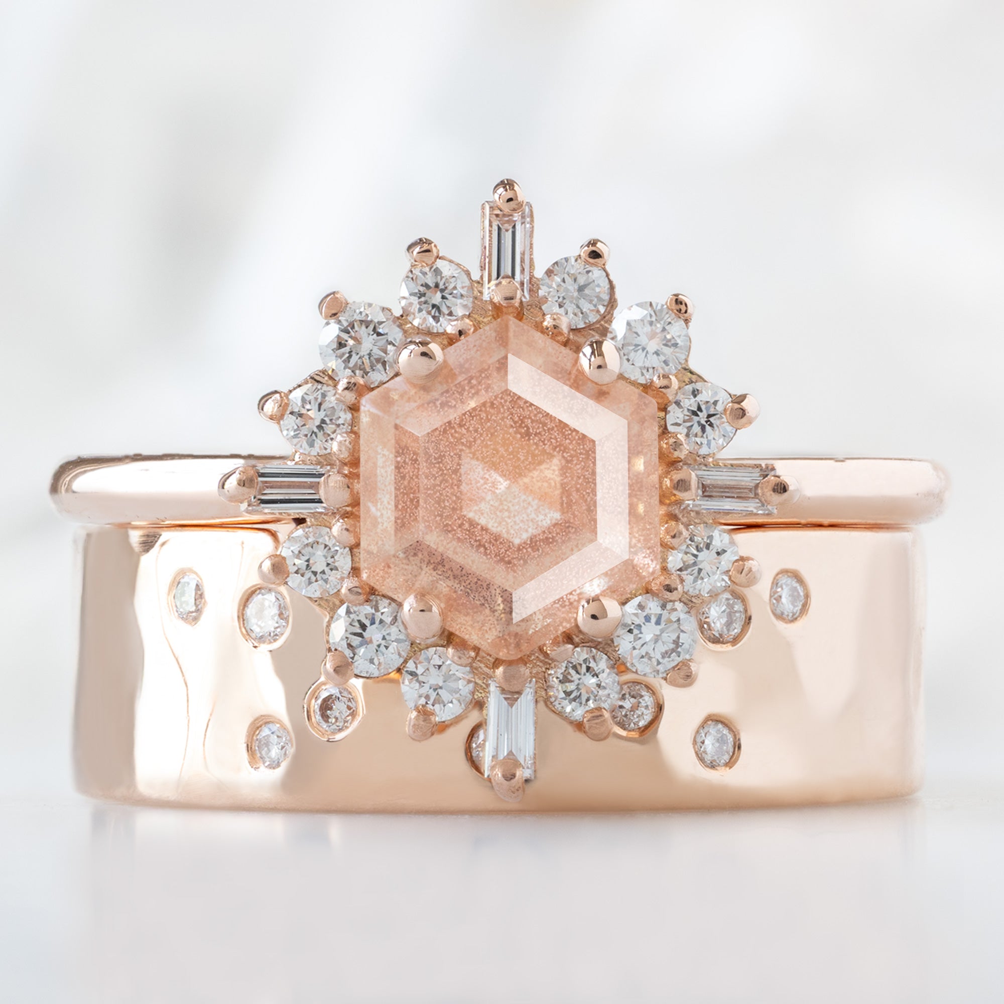 The Compass Ring with a 0.98ct Hexagon Sunstone in 14K Rose Gold Stacked with the Constellation Arc Stacking Band on White Marble Surface