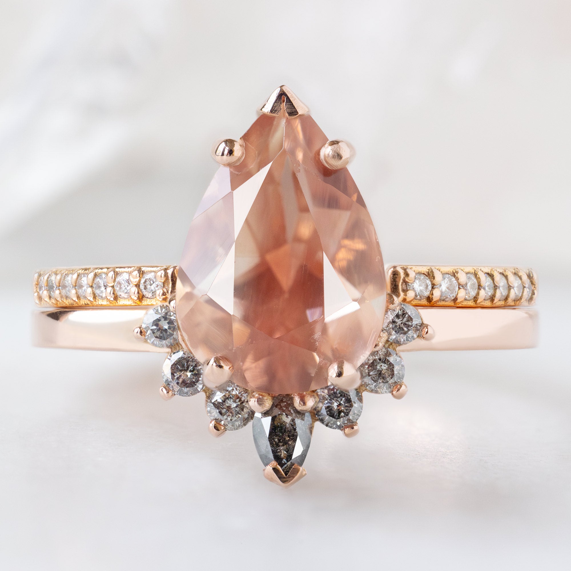 The Aster Ring with a 1.90ct Pear Oregon Sunstone in 14K Rose Gold Stacked with the Open Cuff White Diamond Pavé Stacking Band on White Marble Surface