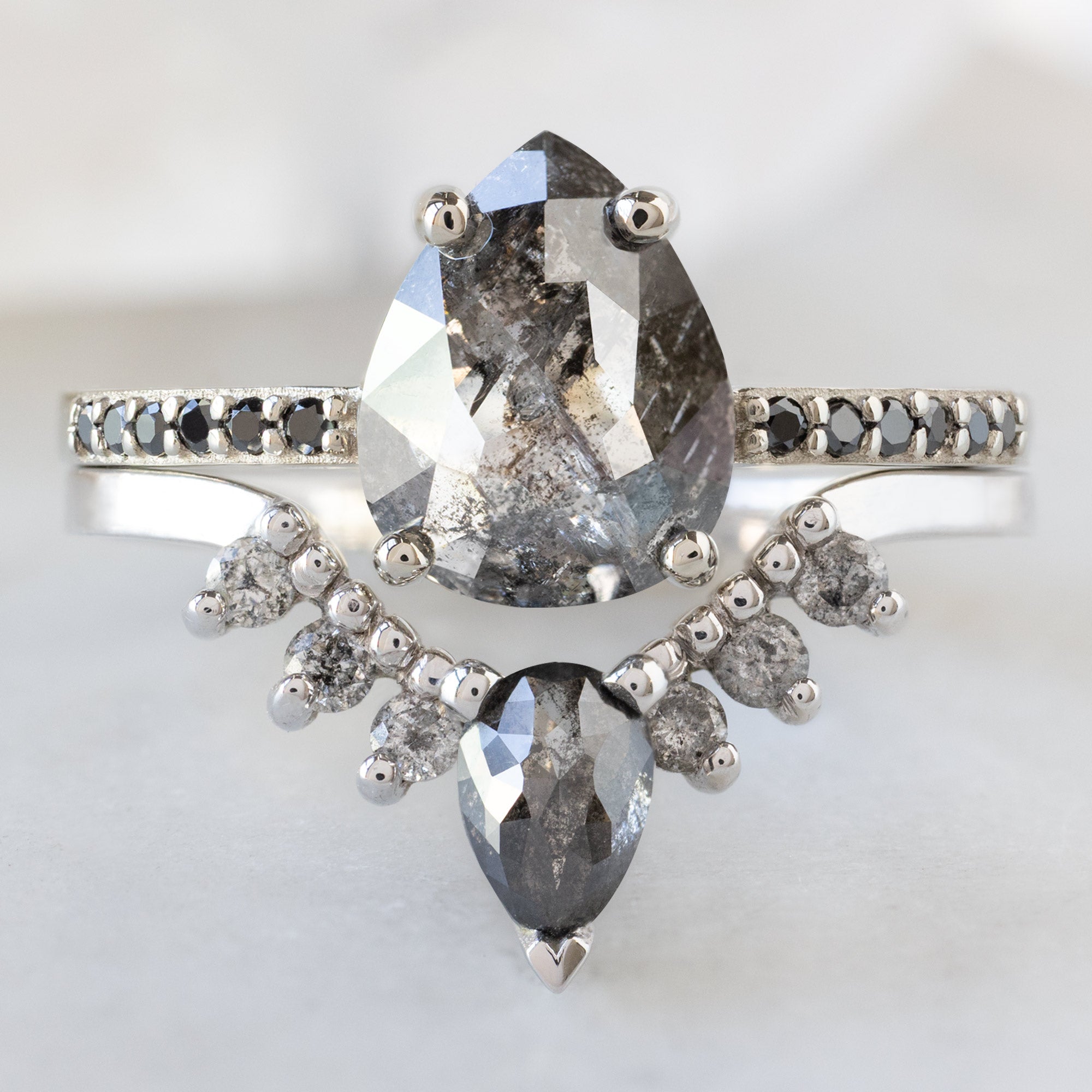 The Willow Ring with a 1.54ct Pear Black Diamond in 14K White Gold Stacked with the Black and Salt and Pepper Diamond Sunburst Stacking Band