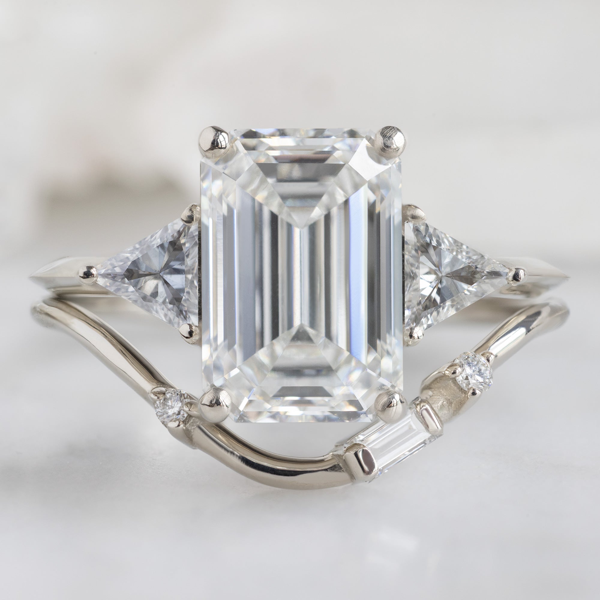 The Jade Ring with a 2.58ct Emerald Cut Lab Grown White Diamond in 14K White Gold Stacked with the Asymmetrical Baguette Diamond Arc Stacking Band on White Marble