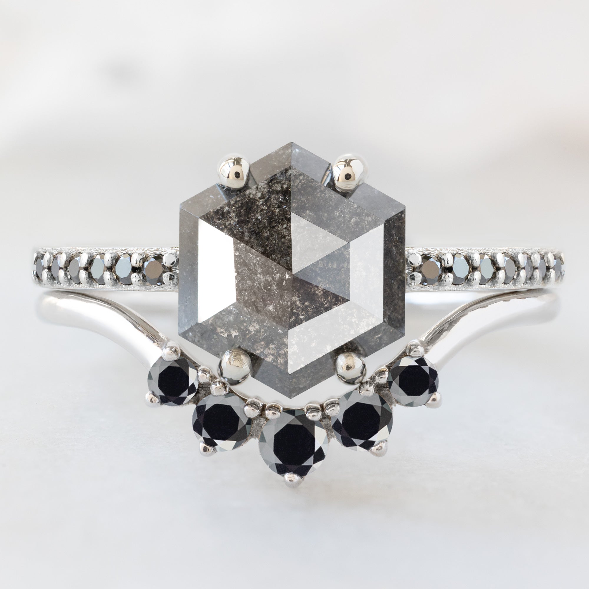 The Willow Ring with a 1.34ct Hexagon Black Diamond in 14K White Gold Stacked with Round Diamond Sunburst Stacking Band on White Marble Surface