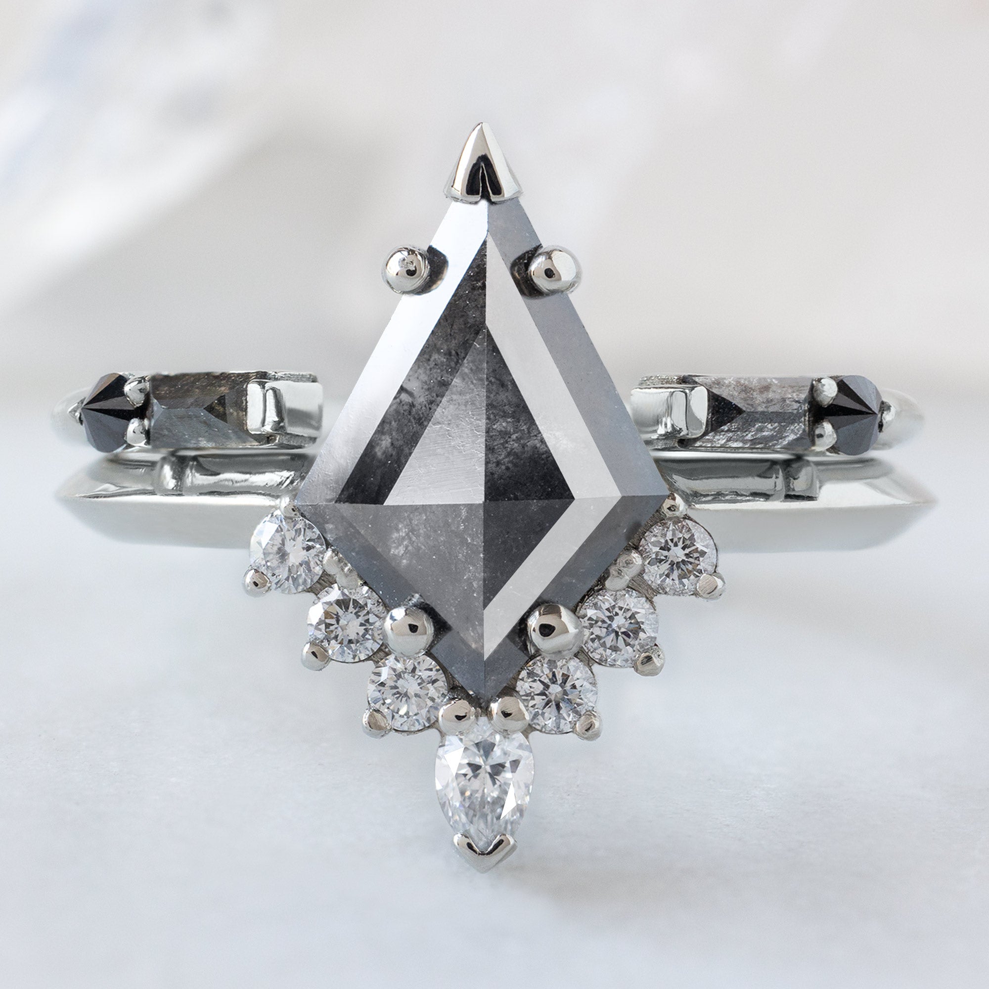 The Aster Ring with a 1.44ct Kite Black Diamond in 14K White Gold Stacked with the Open Cuff Luxe Black Diamond Stacking Band on White Marble Surface