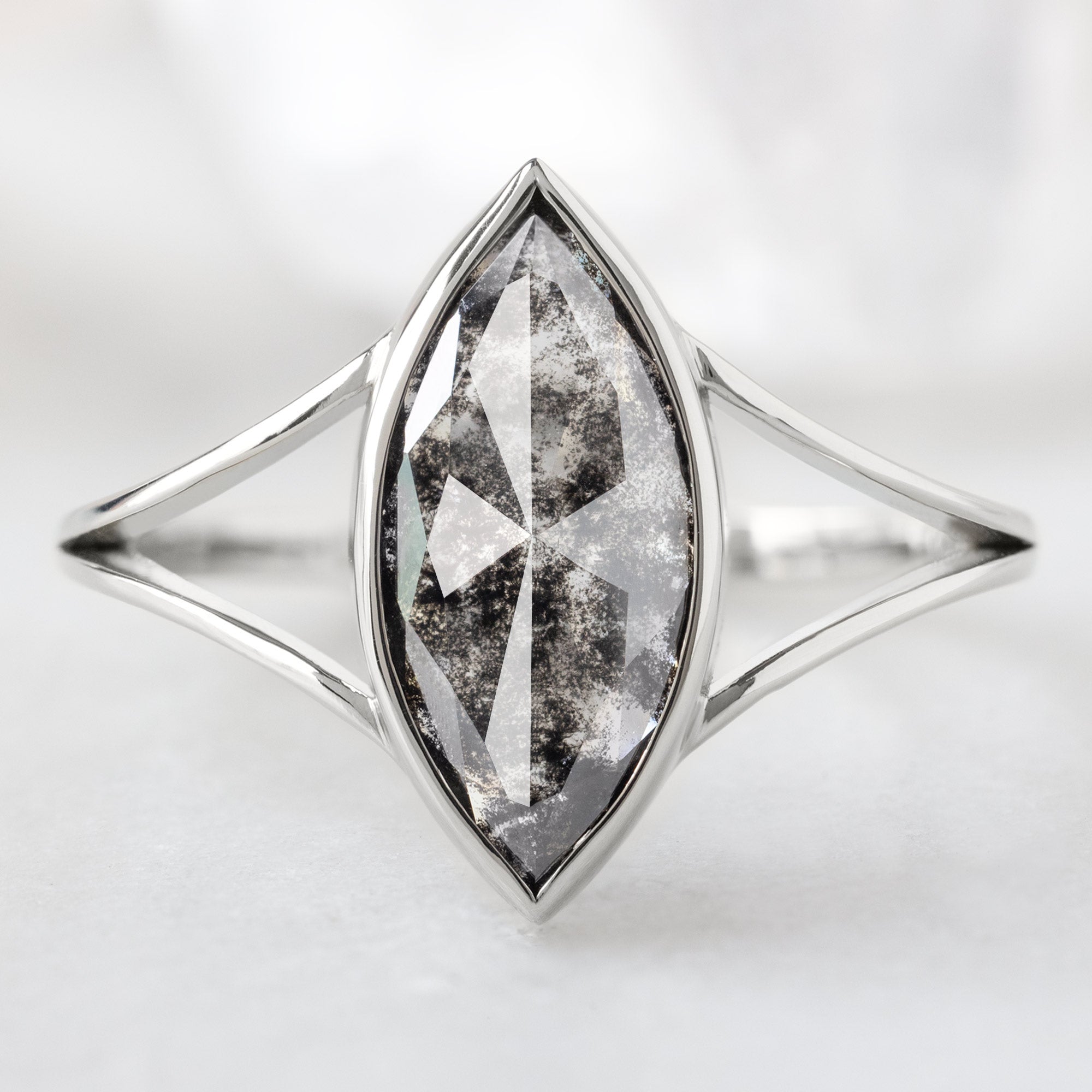 The Magnolia Ring with a 1.68ct Marquise Lab Grown Salt and Pepper Diamond in 14K White Gold on White Marble Background