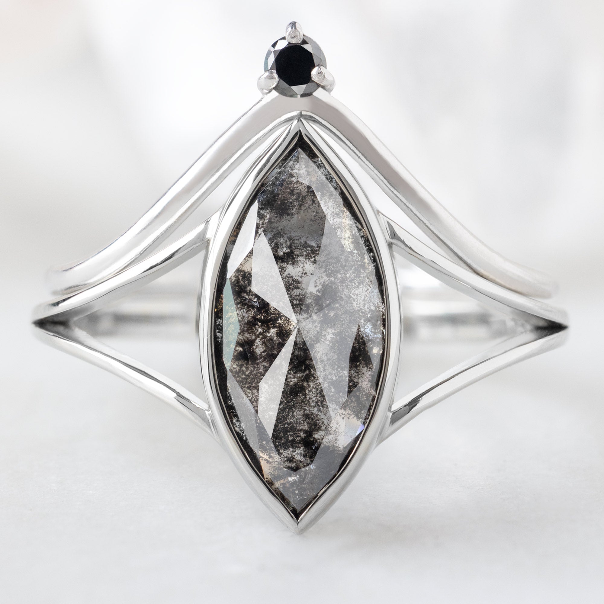 The Magnolia Ring with a 1.68ct Marquise Lab Grown Salt and Pepper Diamond in 14K White Gold Stacked with the Black Diamond Crown Stacking Band on White Marble Background