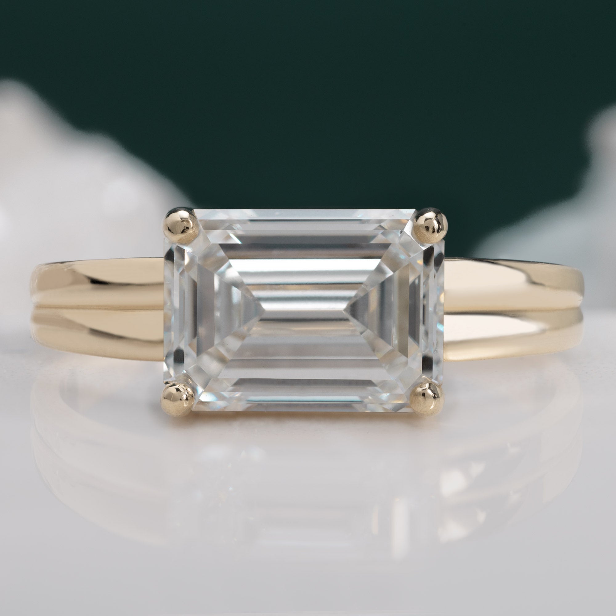 The Stratum Ring with a 1.96ct Emerald Cut Lab Grown White Diamond in 14K Yellow Gold on Green Background