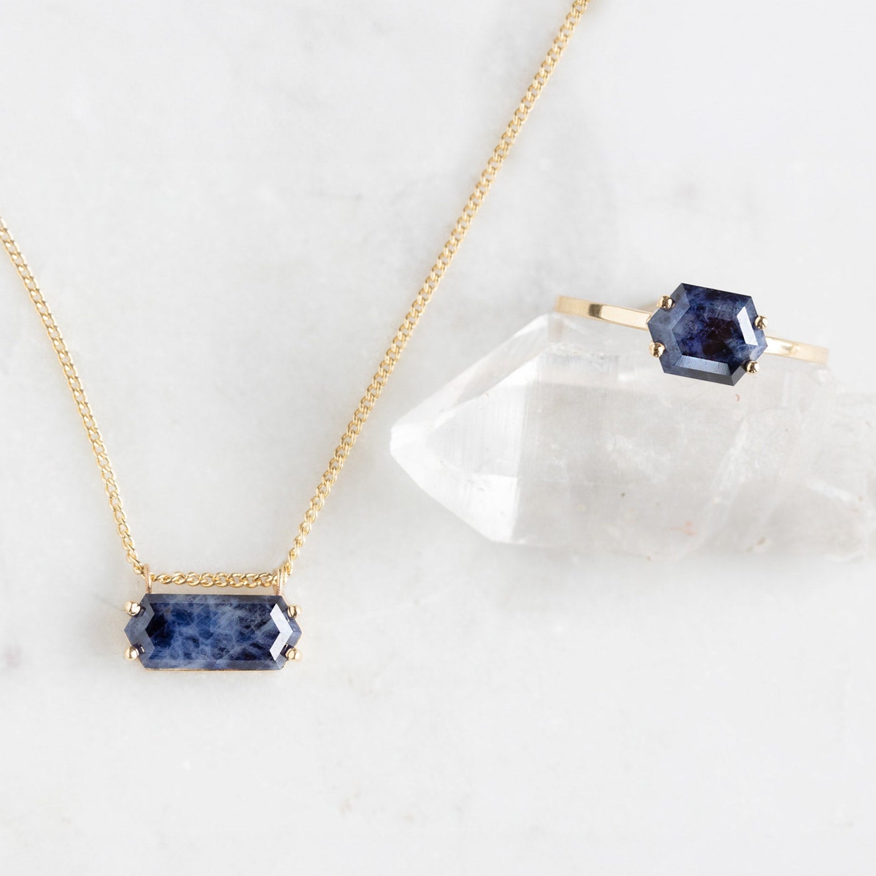 The Raw Sapphire Hexagon Set in Yellow Gold on White Marble Surface