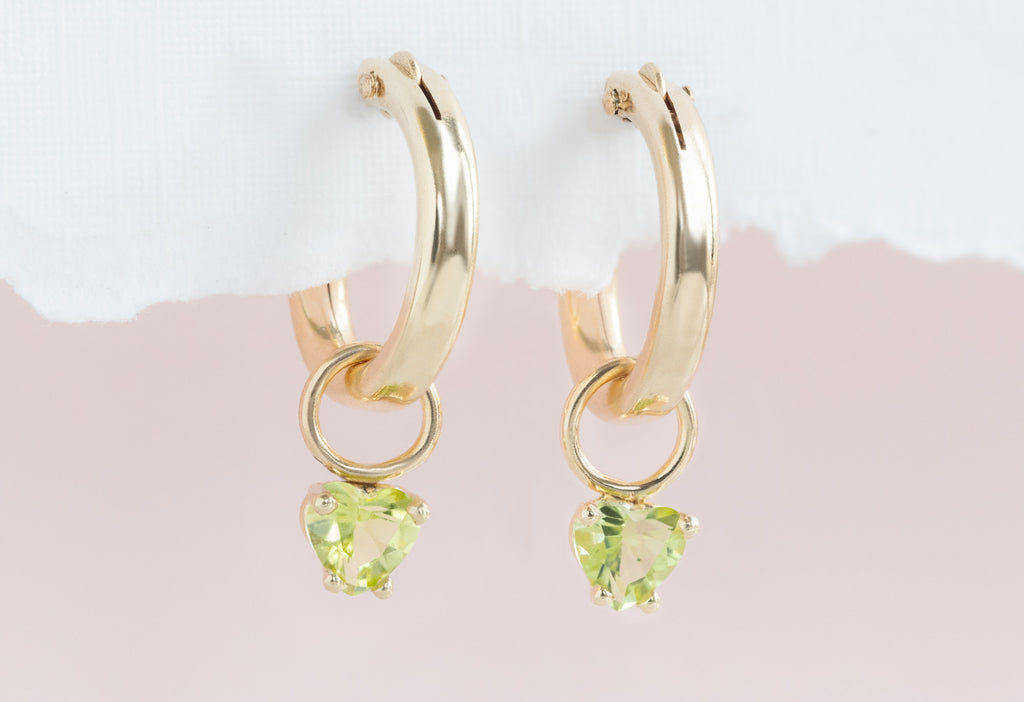 Yellow Gold Peridot Heart Hoops Handing on White Textured Paper with Pink Background