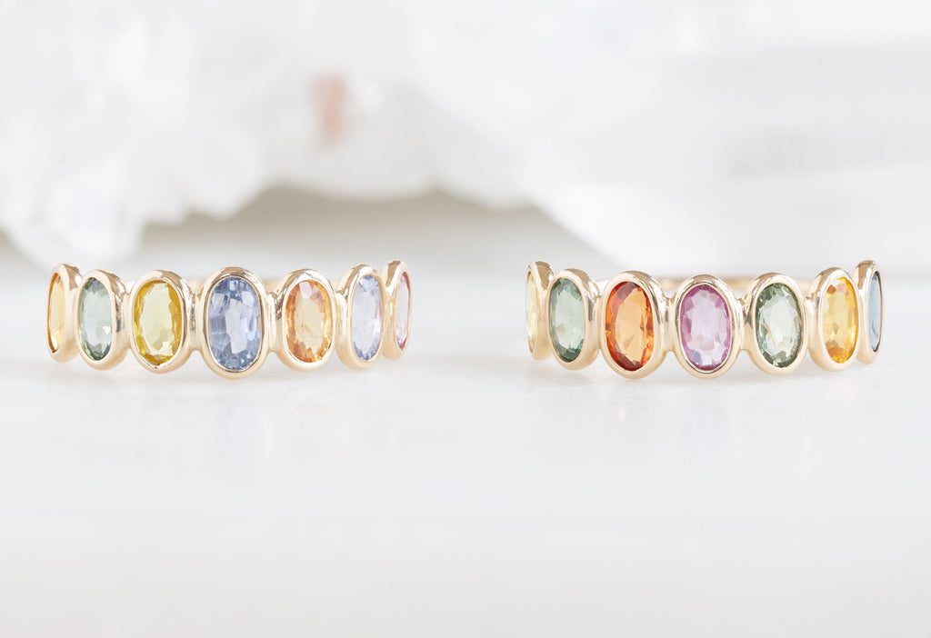 two rainbow sapphire gemstone eternity rings next to each other on white marble tile
