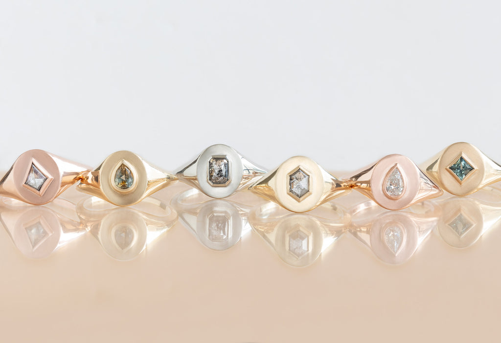  six diamond and gemstone signet rings on peach tile