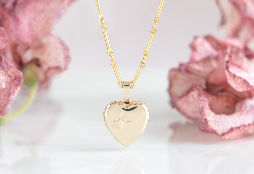 Yellow Gold Sweetheart Diamond Locket Necklace hanging in front of pink flower petals