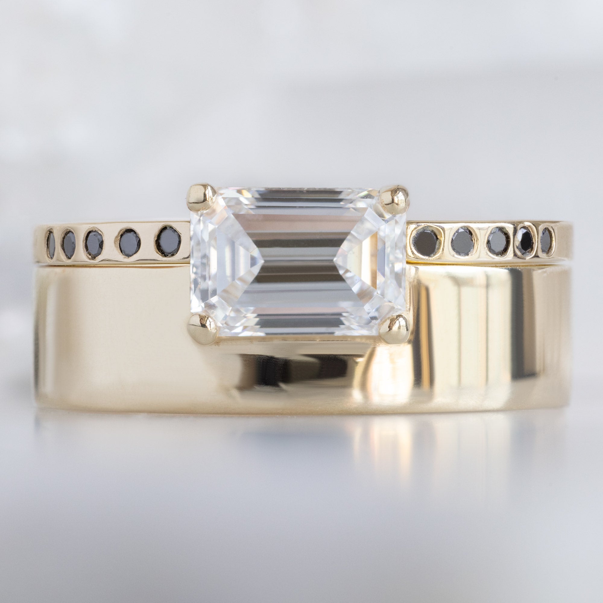 Open Cuff Flush Set Black Diamond Pavé Stacking Band in 14K Yellow Gold Stacked with White Diamond Cigar Band Engagement Ring on White Marble Surface