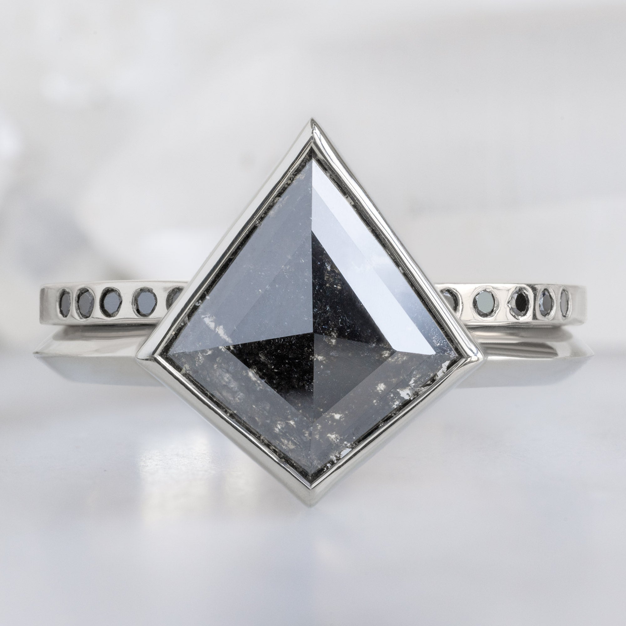 Open Cuff Flush Set Black Diamond Pavé Stacking Band in 14K White Gold Stacked with Black Kite Diamond Solitaire Engagement Ring on White Marble Surface