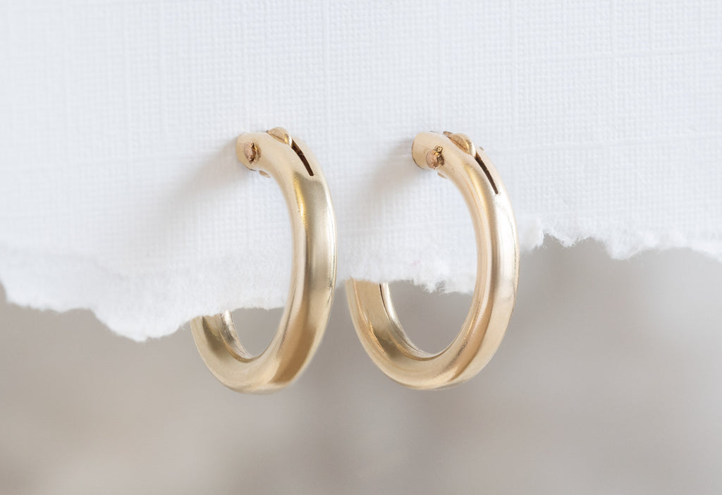 Yellow Gold Charm Hoop Earrings Hanging on White Textured Paper