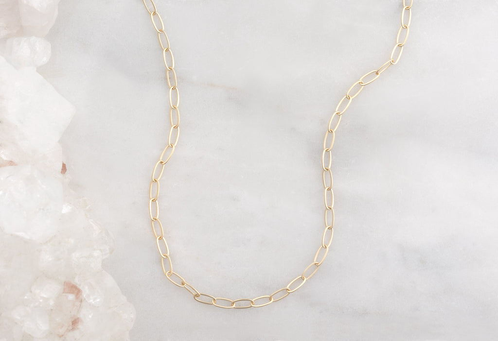 Yellow Gold Drawn Cable Chain Charm Necklace on White Marble Tile