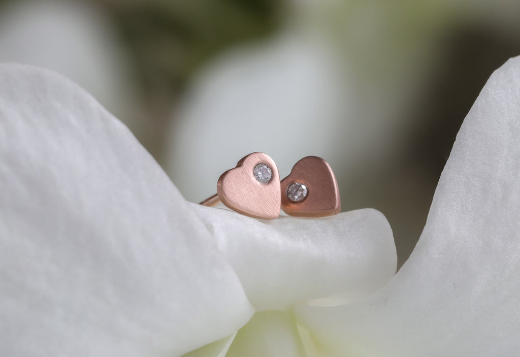 rose gold sweetheart diamond stud earrings laying on white flower petals