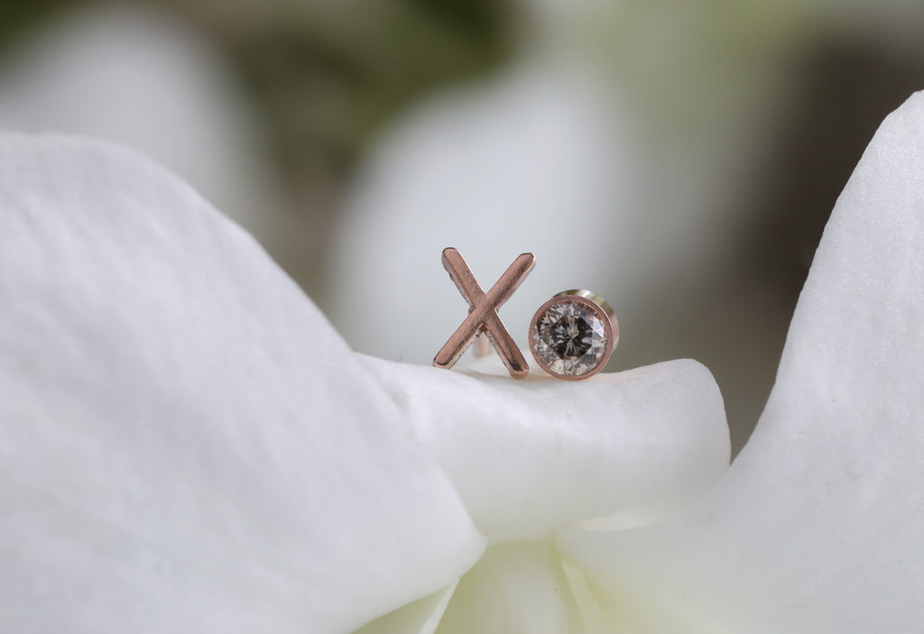 rose gold 'xo' diamond stud earrings laying on white flower petals