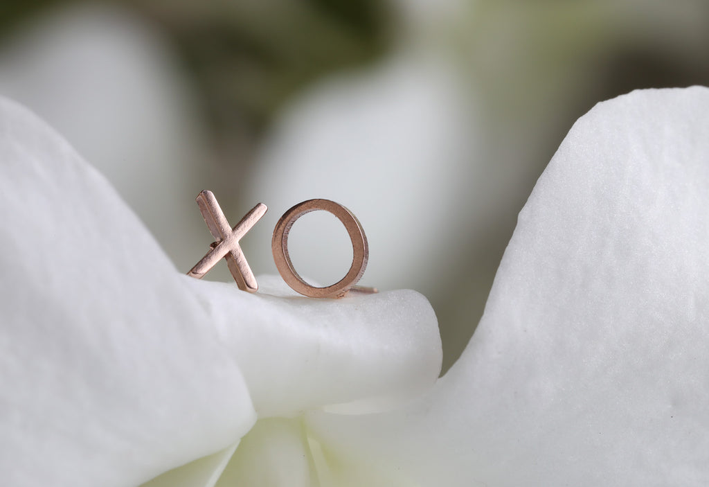 rose gold 'xo' stud earrings laying on white flower petals