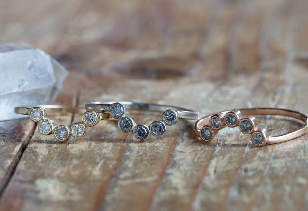 Three Diamond Bezel Arc Rings in yellow, white and rose gold on wood table